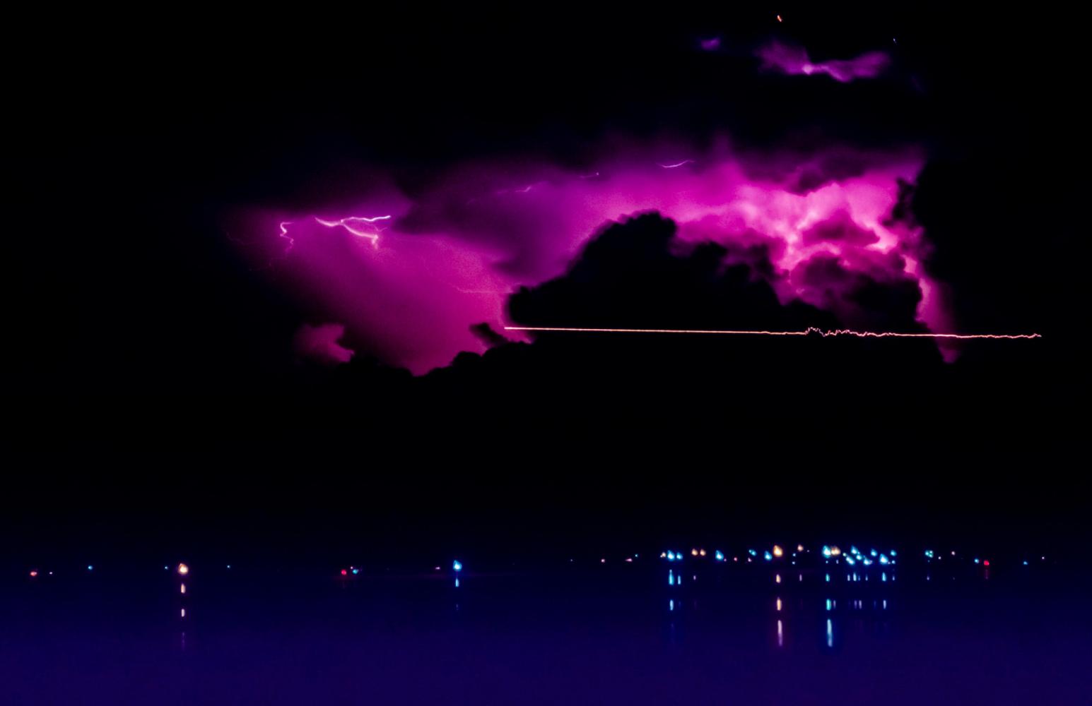 Light trail from aircraft, and distant lightning above the lights of Wellington Point. From Lota.